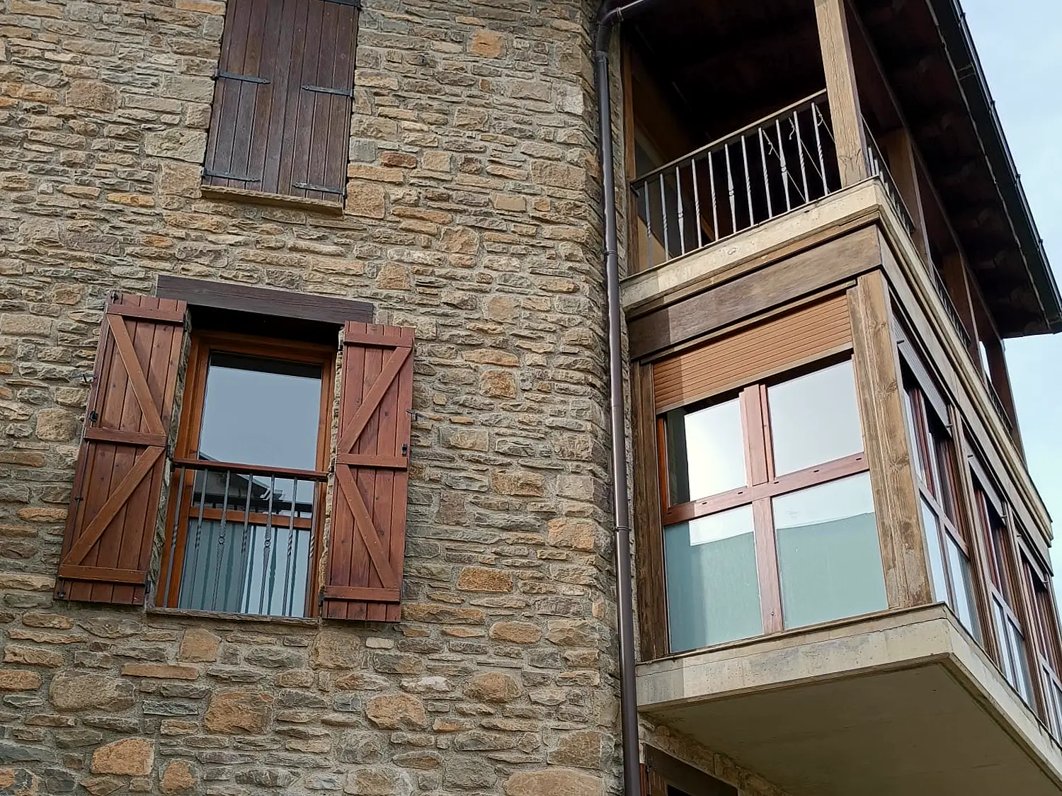 Fachada de piedra rehabilitada con contraventanas de madera en Rada
