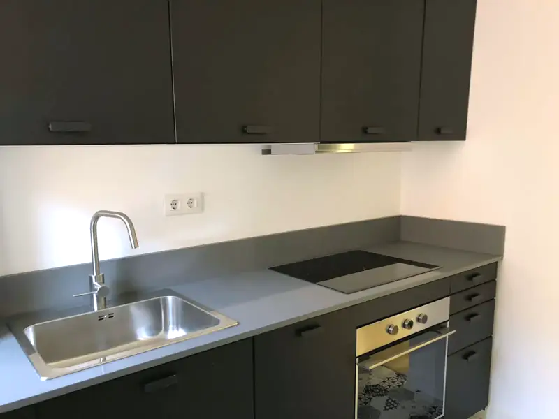 Cocina nueva con frentes oscuros, encimera gris y horno integrado