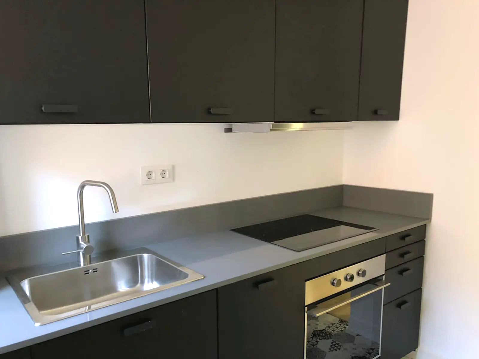 Cocina nueva con frentes oscuros, encimera gris y horno integrado