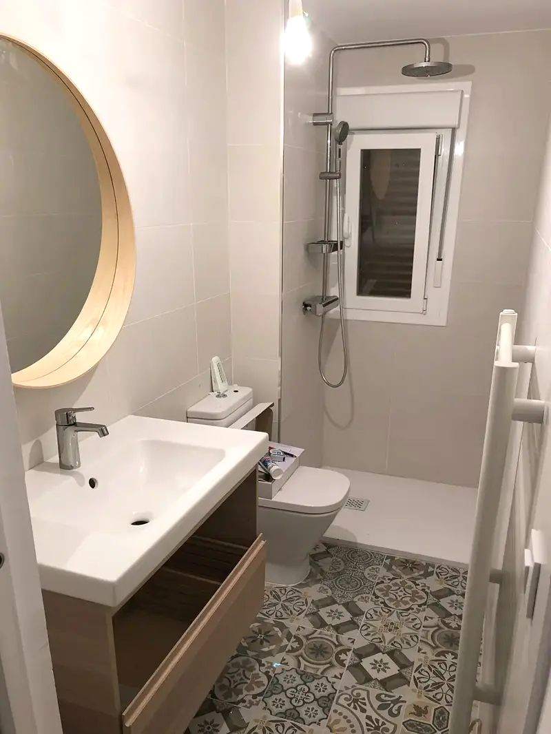 Baño completo con espejo redondo, lavabo y suelo hidráulico