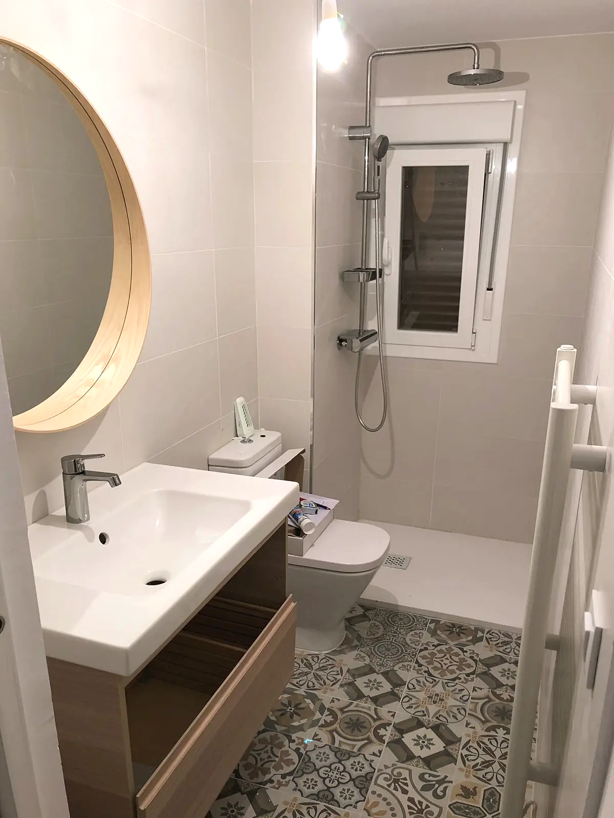 Baño completo con espejo redondo, lavabo y suelo hidráulico
